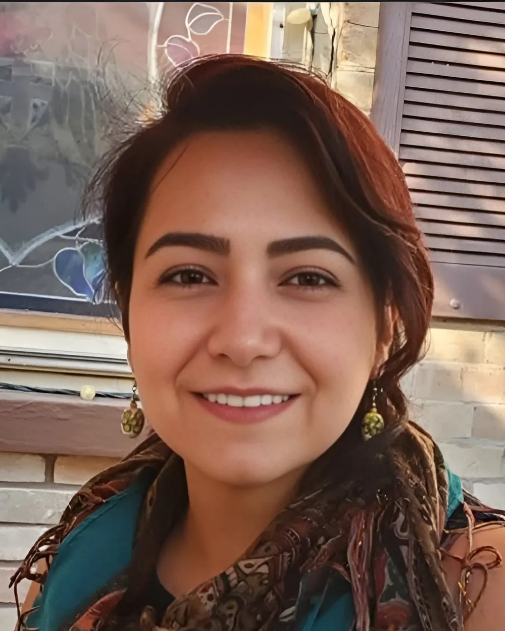 Naz Nezarati, multidisciplinary artist, smiling beside a stained-glass window